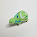 Needle felted wool sculpture of a green rounded body quadruped creature with a cute smile and small black dot eyes. Its body has patterns of clouds, water, and flowers like its a miniature world.