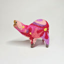 Needle felted wool sculpture of a pink rounded body quadruped creature with an open mouth, goofy smile and small black dot eyes. Its body contains a pink, purple and red retro swirl and floral pattern.