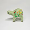Needle felted wool sculpture of a light green rounded body quadruped creature with a cute smile and small black eyes. It has red, orange and yellow poppy flowers on its body.
