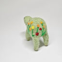 Needle felted wool sculpture of a light green rounded body quadruped creature with a cute smile and small black eyes. It has red, orange and yellow poppy flowers on its body.