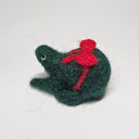 Needle felted wool sculpture of a dark green rounded body quadruped creature with a cute smile and small black eyes. It sits on its hind legs and has a red bow wrapped around its body, as though its a present.
