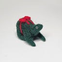 Needle felted wool sculpture of a dark green rounded body quadruped creature with a cute smile and small black eyes. It sits on its hind legs and has a red bow wrapped around its body, as though its a present.