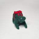 Needle felted wool sculpture of a dark green rounded body quadruped creature with a cute smile and small black eyes. It sits on its hind legs and has a red bow wrapped around its body, as though its a present.