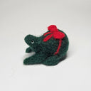 Needle felted wool sculpture of a dark green rounded body quadruped creature with a cute smile and small black eyes. It sits on its hind legs and has a red bow wrapped around its body, as though its a present.