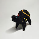 Felted sculpture of a black rounded body quadruped creature with a cute open mouth and bright blue dot eyes. It has a thread of red to orange to yellow ribbon spiraling across its body.