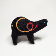 Felted sculpture of a black rounded body quadruped creature with a cute open mouth and bright blue dot eyes. It has a thread of red to orange to yellow ribbon spiraling across its body.