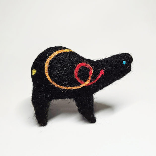 Felted sculpture of a black rounded body quadruped creature with a cute open mouth and bright blue dot eyes. It has a thread of red to orange to yellow ribbon spiraling across its body.