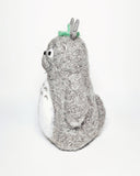 Needle felted wool sculpture of Totoro, standing with a curious expression on his face and arms by his side. He has a leaf atop his head and stiff whiskers.