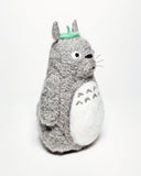 Needle felted wool sculpture of Totoro, standing with a curious expression on his face and arms by his side. He has a leaf atop his head and stiff whiskers.