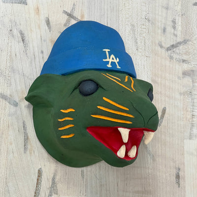 Green panther head sculpture with a blue cap featuring 'LA' on a light wooden background