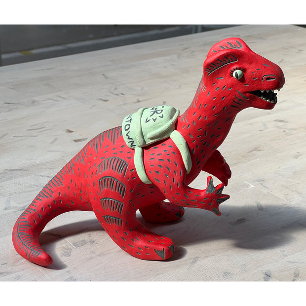 Ceramic sculpture of a red dinosaur wearing a green backpack that says 'GR Japantown"