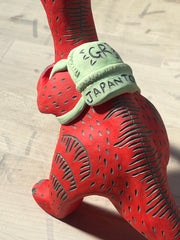 Ceramic sculpture of a red dinosaur wearing a green backpack that says 'GR Japantown"