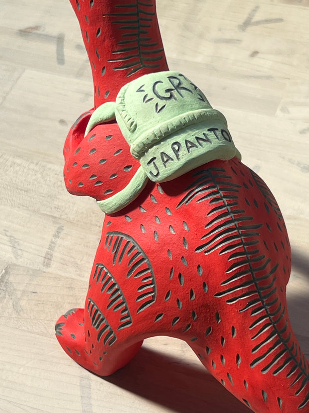Ceramic sculpture of a red dinosaur wearing a green backpack that says 'GR Japantown"