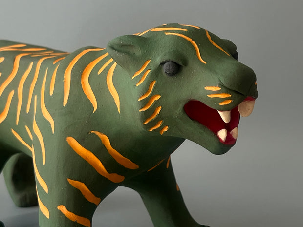 Matte finished ceramic sculpture of a green tiger with orange stripes, it is in a prowling stance with its mouth in a slightly growl.