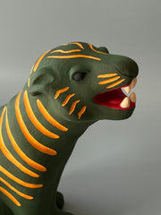 Matte finish ceramic sculpture of a green tiger with orange stripes, sitting on its hindlegs and with an open mouth smile.