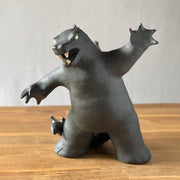 Ceramic sculpture of a large dark gray Godzilla style monster, with his mouth ajar and arms outspread. 