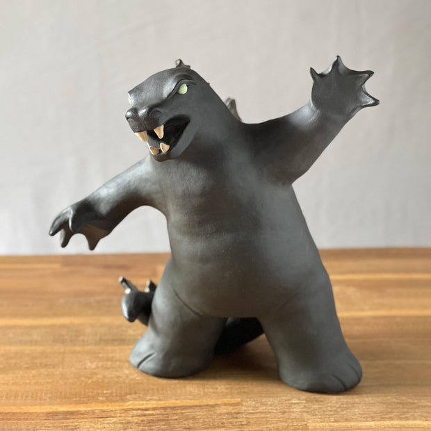 Ceramic sculpture of a large dark gray Godzilla style monster, with his mouth ajar and arms outspread. 