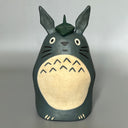 Stylized ceramic figurine of Totoro, standing a smiling with a leaf atop his head.