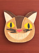 Cat-shaped ceramic coaster with yellow eyes and a pink nose on a wooden surface