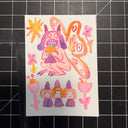 A hand-drawn colorful artwork featuring a whimsical monster, flowers, and three small figures, placed on a black cutting mat with grid lines.