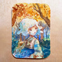A rectangular artwork with rounded corners featuring a watercolor-style illustration of a young girl with curly white hair in an autumn forest. The artwork has warm orange and brown trees against a blue and teal background, placed on a light wood surface.
