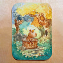 A rectangular watercolor artwork with rounded corners, featuring a whimsical forest scene with a capybara sitting in a wooden tub, trees, and small animals. The print is photographed flat against a light wood background.