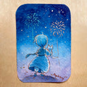 A rectangular artwork with rounded corners featuring a watercolor illustration of a blue-haired girl holding a cat under fireworks at night, displayed on a light wood surface.