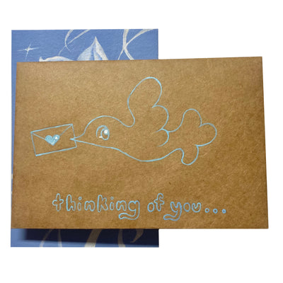 A brown envelope obscuring a blue monochromatic painting. Blue line art on the envelope says "thinking of you.." with a bird holding an envelope.