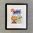 A framed linocut print  of Rugrats with the text 'NO Regrets' on a white mat, set in a black frame against a gray textured fabric background.