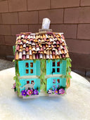 Paper sculpture of a 3D two story house, with shingle roofing, teal colored window shutters and ivy growing along the side. Cats crawl on the flower window boxes and tissues can be pulled from the chimney. 
