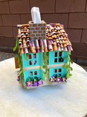 Paper sculpture of a 3D two story house, with shingle roofing, teal colored window shutters and ivy growing along the side. Cats crawl on the flower window boxes and tissues can be pulled from the chimney. 