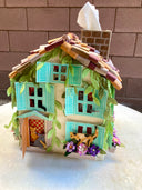 Paper sculpture of a 3D two story house, with shingle roofing, teal colored window shutters and ivy growing along the side. Cats crawl on the flower window boxes and tissues can be pulled from the chimney. 