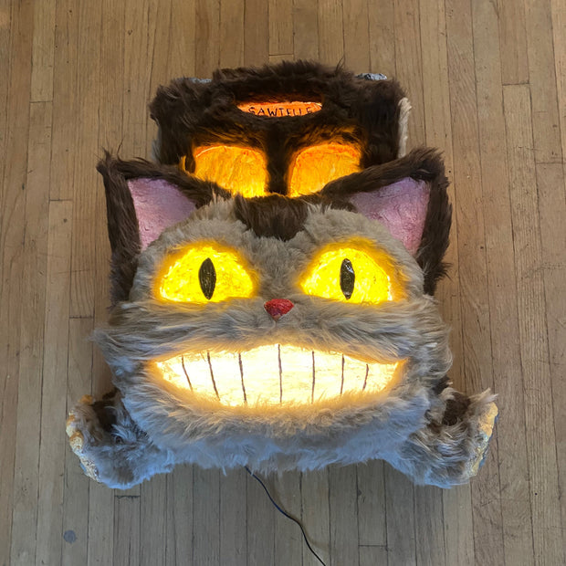 Catbus shaped paper mache and fur wall hanging sculpture, smiling and with lighting elements.