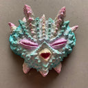 Mask made of paper mache of a pink and blue closed-eyed monster with many spikes and ridges coming off its face.