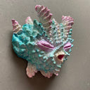 Mask made of paper mache of a pink and blue closed-eyed monster with many spikes and ridges coming off its face.