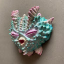 Mask made of paper mache of a pink and blue closed-eyed monster with many spikes and ridges coming off its face.