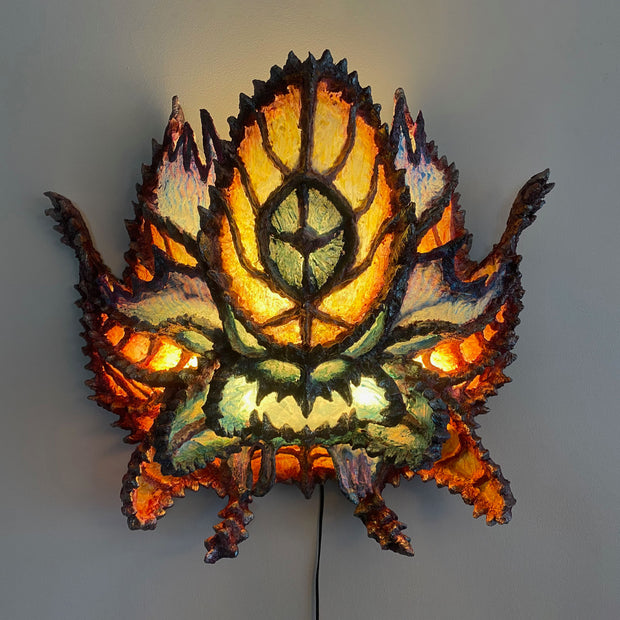Sculpture of a monster's head, made out of paper mache and colored in blues and warm tones with a light shining through it, casting an ambient glow.