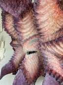 Very large paper mache sculpture of a monster's head with many pointed edges, akin to a leaf with a menacing face.