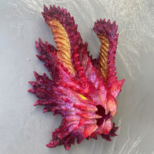 Paper mache sculpture of a pink kaiju monster's head - with a beak like mouth and 2 large ears that protrude upwards like horns.