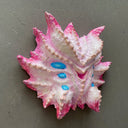 Mask made of paper mache of a pink and white multi-eyed monster with many spikes coming off its face.