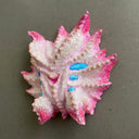 Mask made of paper mache of a pink and white multi-eyed monster with many spikes coming off its face.