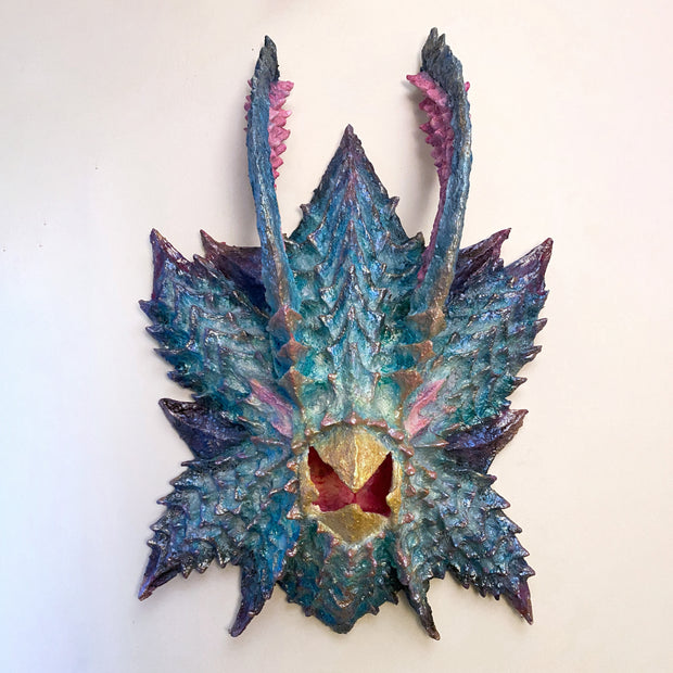 Paper mache sculpture of a monster's head without facial features aside from an open mouth beak.