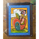 A colorful hand-drawn artwork featuring a whimsical fairy-like character standing on a red heart-shaped house, photographed flat on a worn wooden surface.