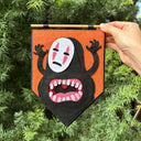 Hand holding a decorative banner with a stylized face design against a green leafy background