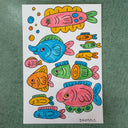 Collection of doodles done in marker on a sheet of sketchbook paper - several colorful fish with cute cartoon faces and accentuated shapes.