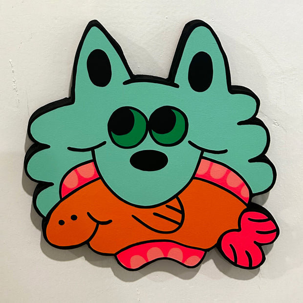 Die cut wooden panel in the shape of a cartoon cat head, painted a teal green color. It has green eyes and looks off to the side, holding an orange fish in its mouth.