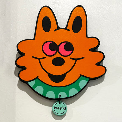 Die cut wooden panel in the shape of a cartoon cat head, painted bright orange with stark black outlines. It has red eyes and smiles, wearing a green collar with a circle charm hanging off that says Dreyfus.