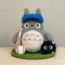 Crocheted Totoro character with a baseball cap, baseball bat and baseball on a green base. Next to him is a soot sprite character.