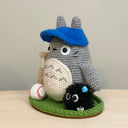 Crocheted Totoro character with a baseball cap, baseball bat and baseball on a green base. Next to him is a soot sprite character.