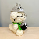 Fluffy plush sculpture of a white dog with black beaded eyes and wire framed glasses. It wears a green scarf and has a camera around its neck and a Totoro hat.